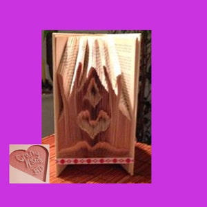 May include: A decorative book art piece with folded pages, creating a design. The book is beige with a red and white patterned ribbon at the base. The design features a central heart shape and other geometric elements.