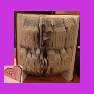 May include: An open book with the words "LET THE ADVENTURE BEGIN" carefully folded into the pages. A small silver object is placed within the folded pages. A heart-shaped logo with the words "Crafty Home" is in the corner of the image.