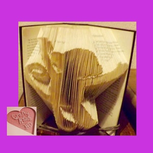 May include: A book art sculpture of a face created by folding the pages of a book. The sculpture is made from a book with a brown cover. The sculpture is on a table.