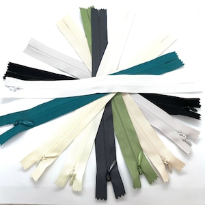May include: Assortment of 12 zipper closures in various colours, including white, black, green, and teal. The zippers are laid out in a circular pattern on a white surface.