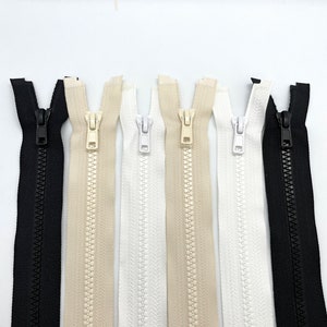 May include: Six zipper closures in various colours, including black, beige, and white. The zippers are all closed and have a metal slider.