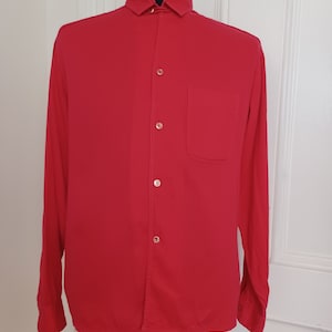May include: A long-sleeved, button-down shirt in a bright red color. The shirt has a single pocket on the left chest.