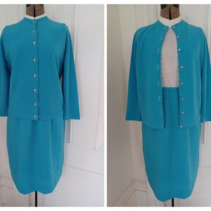 May include: A turquoise blue knit skirt suit with a cardigan and skirt. The cardigan has a scalloped edge and buttons down the front. The skirt is a straight silhouette.