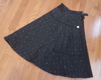 May include: A black skirt with a white flecked pattern. The skirt has a high waist and a flared silhouette. It features a single button closure and a small pocket on the side.