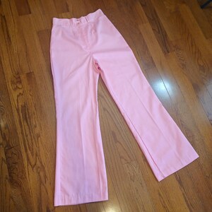 May include: A pair of light pink pants with a flared leg design. The pants have a button and zipper closure, belt loops, and front pockets. The pants are made of a smooth, solid-colored fabric.