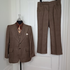 May include: A brown plaid suit, consisting of a jacket, vest, and pants. The jacket is displayed on a mannequin, paired with a brown shirt and patterned tie. The pants hang on a hanger. The suit is a classic style.
