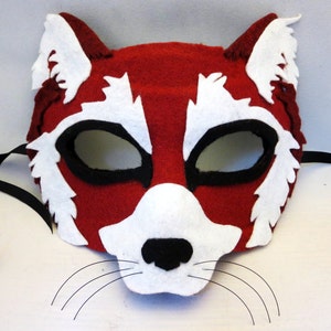 May include: Red and white felt animal mask with black eye holes and a black felt nose. The mask has white felt whiskers and a black felt ribbon for tying.