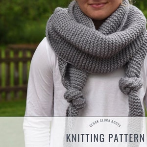 May include: A gray knitted scarf with a knotted fringe. The scarf is worn by a person and is draped around their neck. The text "Cluck Cluck Boots Knitting Pattern" is visible at the bottom of the image.