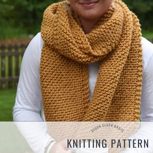 May include: A mustard yellow knitted scarf with a simple stitch pattern. The scarf is worn by a person in a white shirt. The image includes the text "Cluck Cluck Boots Knitting Pattern".