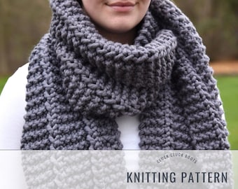 May include: A gray knitted scarf with a textured pattern. The scarf is folded and worn around the neck of a person. The text "Cluck Cluck Boots Knitting Pattern" is visible at the bottom of the image.