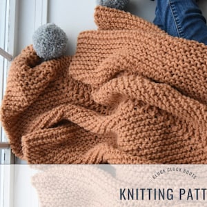 Puede incluir: Una manta de punto marrón con pompones en las esquinas. La manta está doblada y drapeada sobre un par de vaqueros. El texto "CLUCK CLUCK BOOTS KNITTING PATTERN" está impreso sobre un fondo blanco debajo de la manta.