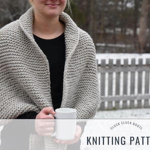 May include: A gray knitted shawl with a cowl neck, worn by a person holding a white mug. The text "Cluck Cluck Boots Knitting Pattern" is at the bottom of the image.