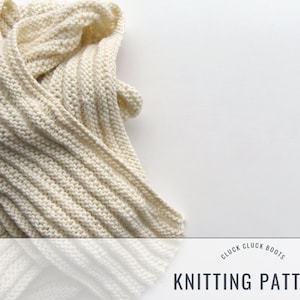 Puede incluir: Primer plano de una bufanda de punto de color crema con textura de canalé. La bufanda está doblada y drapeada sobre una superficie blanca. El texto "CLUCK CLUCK BOOTS KNITTING PATTERN" está impreso debajo de la bufanda.