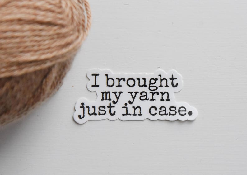 May include: A sticker with the text "I brought my yarn just in case" in black font. A ball of tan yarn is in the upper left corner. The sticker and yarn are on a white surface.