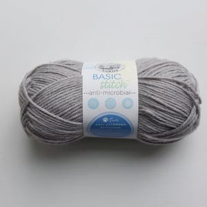 May include: A skein of gray yarn with a label that reads "Basic Stitch" and "anti-microbial". The yarn is a light gray color and appears to be soft. The label also indicates that the yarn is anti-allergen.
