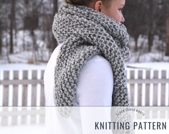May include: A gray and white chunky knit scarf with a textured stitch pattern. The scarf is worn by a person in a white shirt. The image includes the text "Cluck Cluck Boots Knitting Pattern".