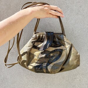 Puede incluir: Un bolso de mano de cuero marrón con un diseño de patchwork único que presenta patrones de cocodrilo, serpiente y malla. El bolso tiene un asa superior y una correa larga.