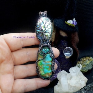 Puede incluir: Un colgante envuelto en alambre de cobre con una piedra turquesa verde y azul y un diseño de árbol de la vida con concha de abulón. El colgante cuelga de un bucle de alambre de cobre.