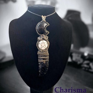 May include: A black obsidian pendant necklace with a wire-wrapped pentagram charm and a crescent moon charm. The necklace is on a black display stand with the text "Charisma Crystals" below the stand.