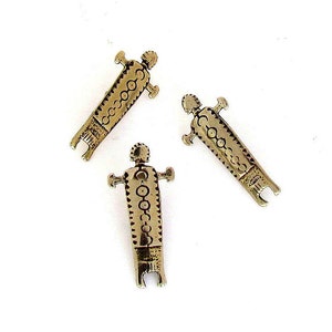 May include: Three gold-colored metal figurines of people with intricate designs. The figurines are standing upright and have a stylized appearance.
