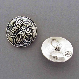 May include: A pair of silver-toned metal buttons with a raised design of pine cones. The front of the button features a detailed design of two pine cones with branches. The back of the button is smooth and has a small hole for sewing.