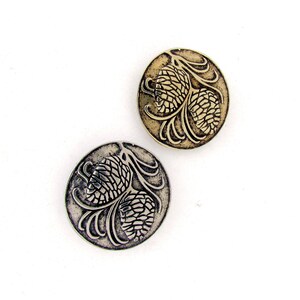 May include: Two silver-toned metal buttons with a raised design of pine cones. The buttons are round and have a detailed design of two pine cones with branches.