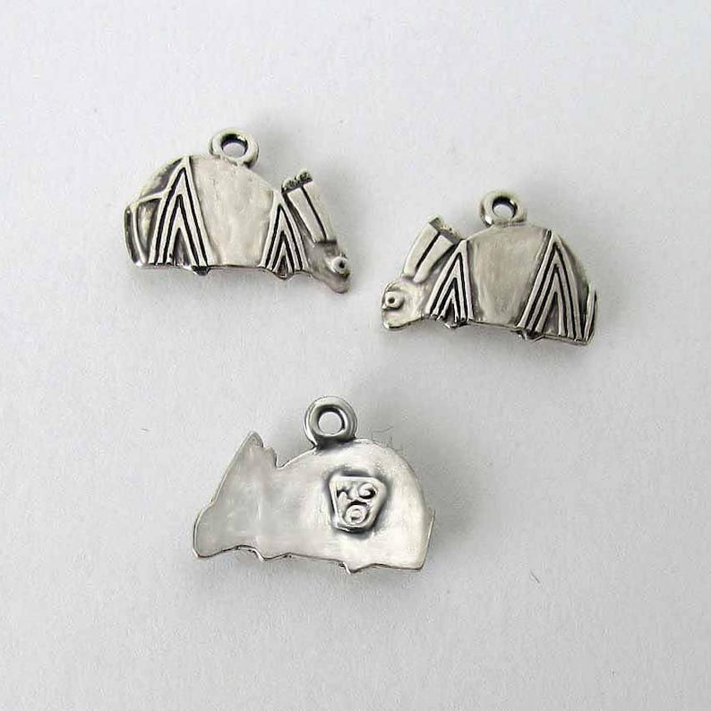May include: Three silver charms in the shape of a bat. The charms are detailed with intricate wing patterns and have a small loop for attaching to a necklace or bracelet.