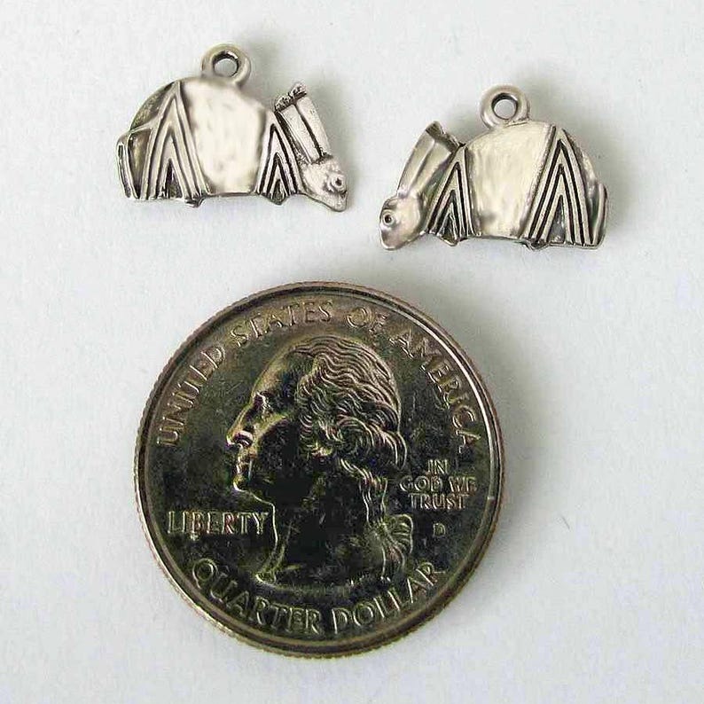 May include: Two silver bat charms with detailed wings and a textured surface. The charms are shown next to a US quarter for size reference.