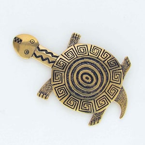 May include: A gold-toned metal turtle brooch. The turtle's shell features a spiral and square pattern, with a zig-zag design on the neck. The head has two circular eyes and a rectangular mouth. The legs are stylized.