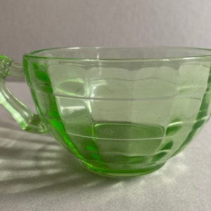 May include: A green glass teacup with a handle. The cup has a textured, geometric design.