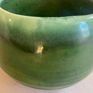 May include: A green ceramic bowl with a glossy finish. The bowl has a rounded shape and a slightly flared rim.