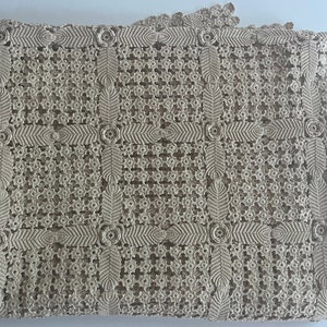 May include: A beige crocheted tablecloth with a delicate floral pattern. The tablecloth features a repeating design of small flowers and leaves.