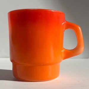 May include: A vibrant orange mug with a rounded handle. The mug features a gradient color, transitioning from a deep red at the top to a bright orange at the base. The mug has a stacked design.