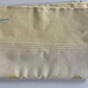 May include: A folded yellow and white fabric with a label that reads "100% Baumwolle".