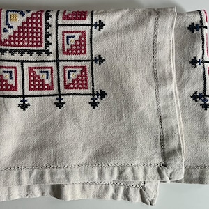 May include: A white linen tablecloth with a black and red embroidered design. The embroidery features geometric shapes and a repeating pattern.
