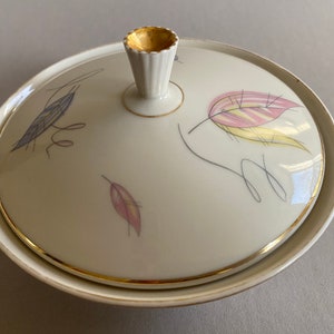 May include: A white ceramic sugar bowl with a lid. The lid has a gold trim and a gold knob. The bowl has a floral design with pink, yellow, and blue accents.