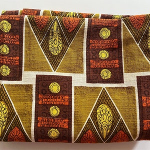 May include: A brown and green fabric with a geometric pattern. The pattern features repeating shapes of diamonds, squares, and rectangles. The fabric has a textured surface.