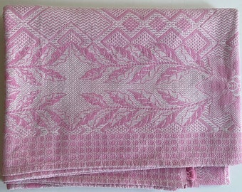 May include: A pink woven tablecloth with a white floral pattern. The tablecloth has a diamond pattern border.