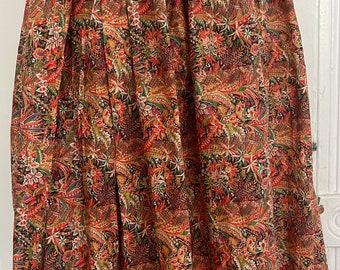 May include: A vintage skirt with a colorful floral pattern. The skirt features a high waist and a full, pleated design. The fabric showcases a mix of red, green, brown, and gold hues, creating a vibrant and eye-catching look. The skirt is displayed on a mannequin.