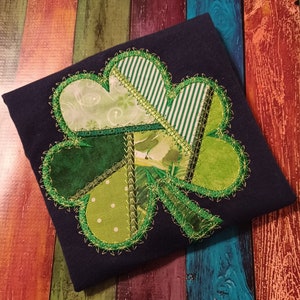 May include: A navy blue t-shirt with a green, white, and brown patchwork shamrock design.