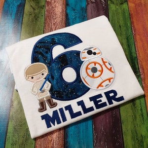 May include: White t-shirt with a blue number six with a galaxy design, a white and orange BB-8 character, a cartoon Luke Skywalker character, and the name "MILLER" in blue.