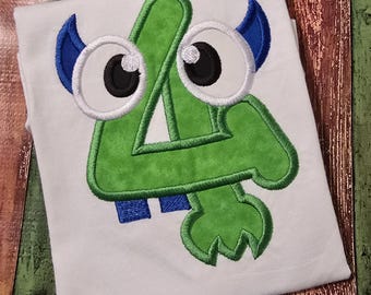 May include: A white t-shirt featuring a large, green embroidered number four designed to look like a monster. The design includes two large white eyes with black pupils, two blue horns at the top, and two small blue teeth at the bottom.