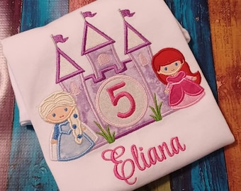 May include: White t-shirt with an embroidered purple castle, two princesses, and the number 5. The name "Eliana" is embroidered below the castle.
