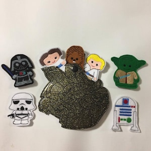May include: A set of felt finger puppets featuring characters from Star Wars. The puppets include Darth Vader, a Stormtrooper, Chewbacca, Princess Leia, Luke Skywalker, Yoda, and R2-D2. The puppets are all in a cartoon style and are brightly colored.