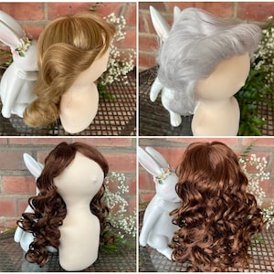 May include: Three mannequin heads with different hairstyles. The heads are wearing wigs in blonde, silver, and brown. Each head is wearing a white rabbit figurine.