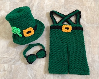 May include: A green crocheted leprechaun costume for a baby, including a hat, overalls, and a bow tie.