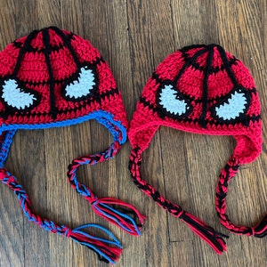 May include: Two crocheted hats with black and red stripes and white eyes. The hats have long ties that are black, blue, and red.