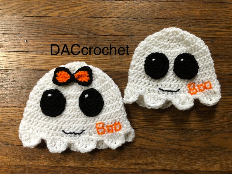May include: Two crocheted ghost hats, one with an orange bow and the other with the word "Boo" embroidered on it. Both hats have black eyes and a white crocheted face.