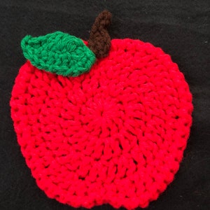 Puede incluir: Una manzana roja de ganchillo con una hoja verde y un tallo marr&oacute;n. La manzana est&aacute; hecha con punto bajo y tiene una superficie texturizada.