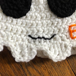 May include: White crocheted ghost hat with black eyes and a stitched-on black mouth. The hat has a scalloped edge.